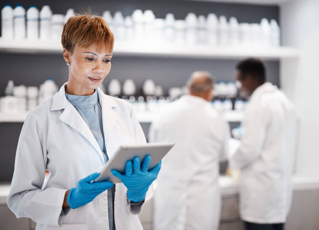 Scientist in lab coat wearing gloves looks at a tablet